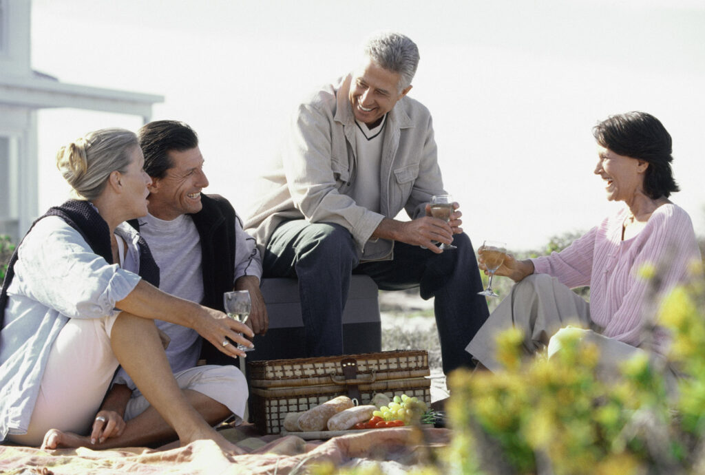 Invecchiamento e Salute: coppie di mezza età durante un pic-nic in spiaggia che sorridono felici